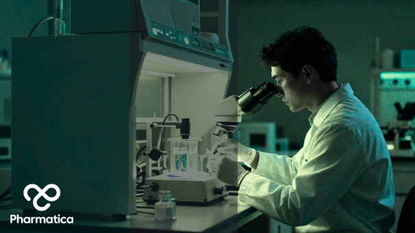 A scientist in a lab coat and gloves looking through a microscope at a workstation, with the Pharmatica logo in the bottom left corner.